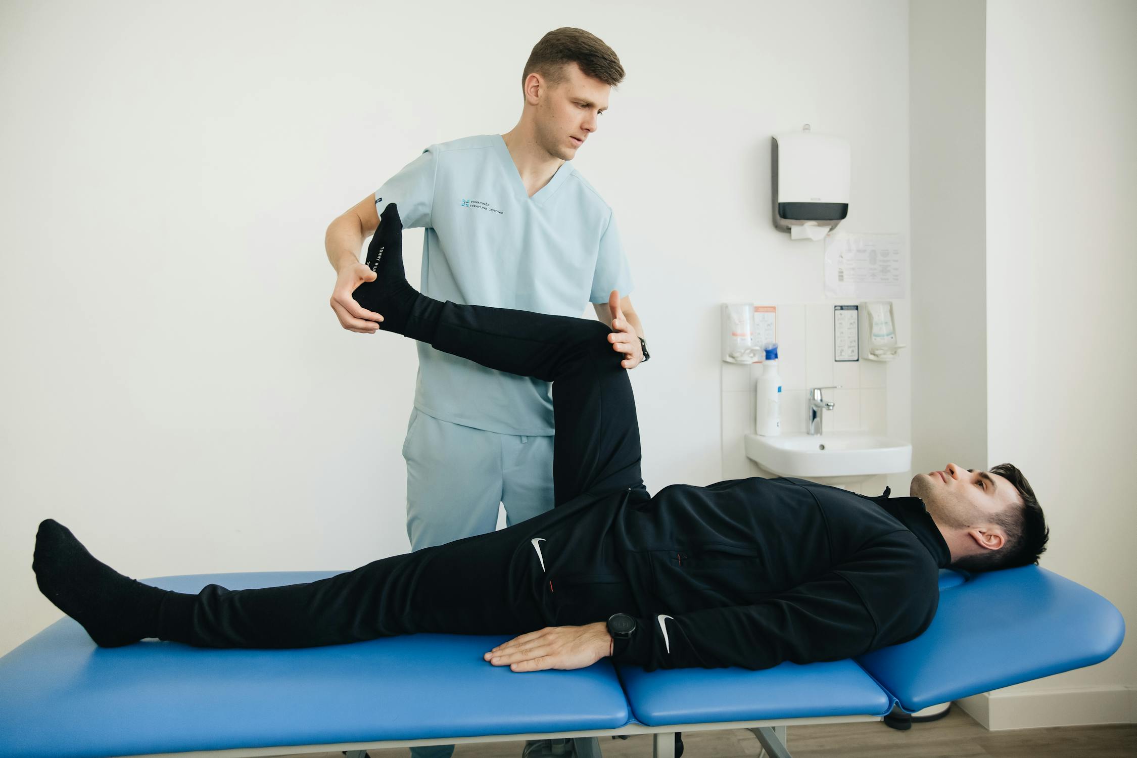 Physiotherapist assisting a patient with leg rehabilitation exercises on a therapy table in a clinical setting.