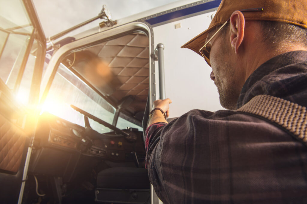 A weary truck driver climbing up into the cab of a semi-truck at sunset