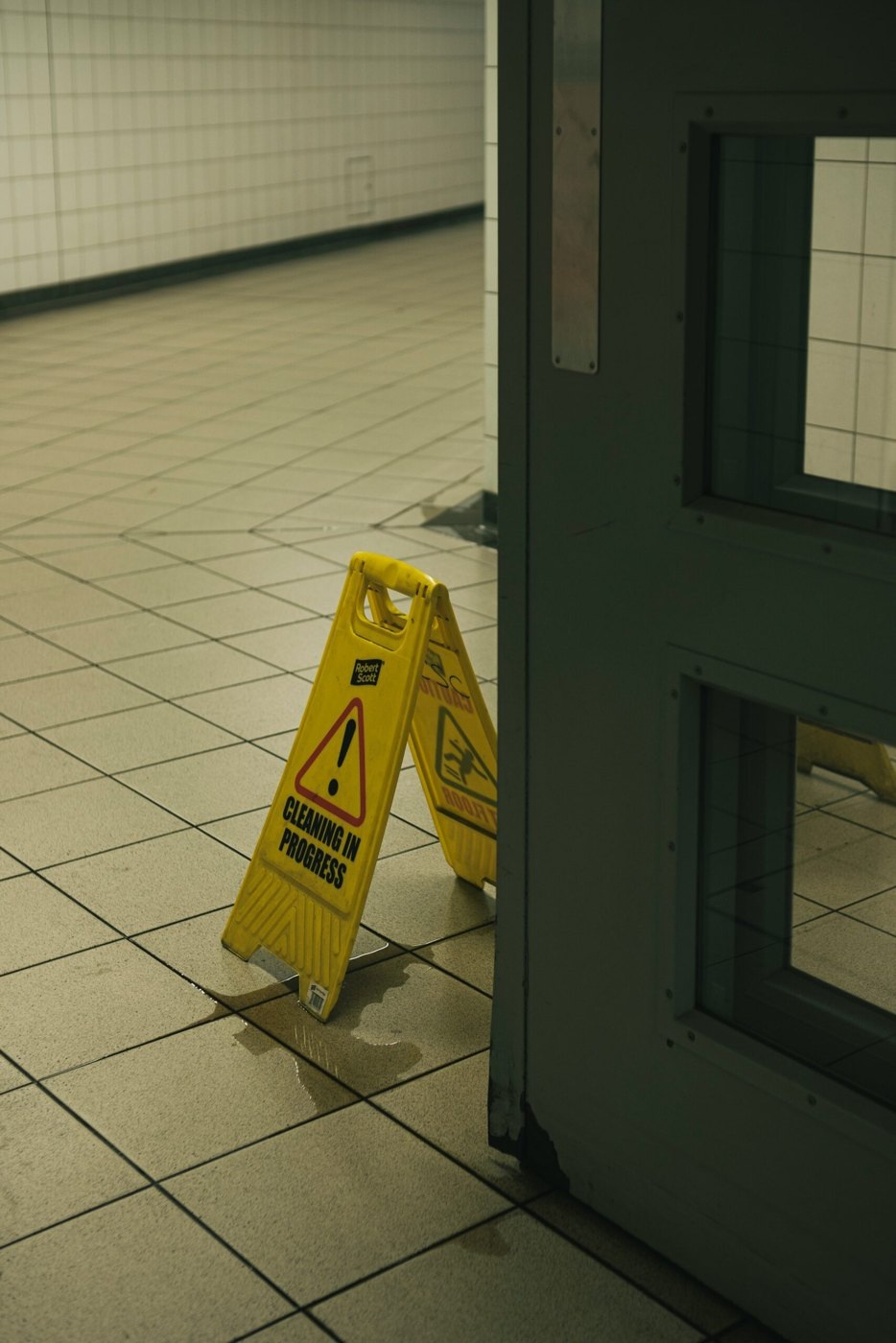 Yellow cleaning-in-progress sign beside a wet tiled floor and doorway